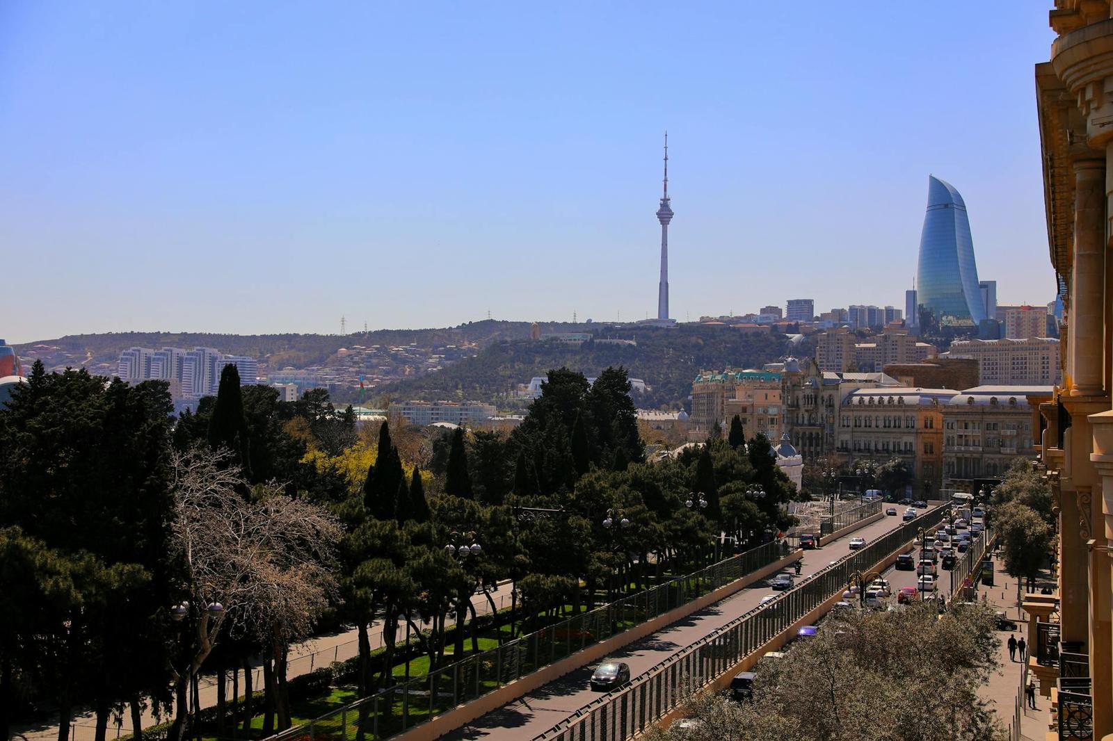 A tree-lined boulevard leads toward a distant television tower and glass skyscraper