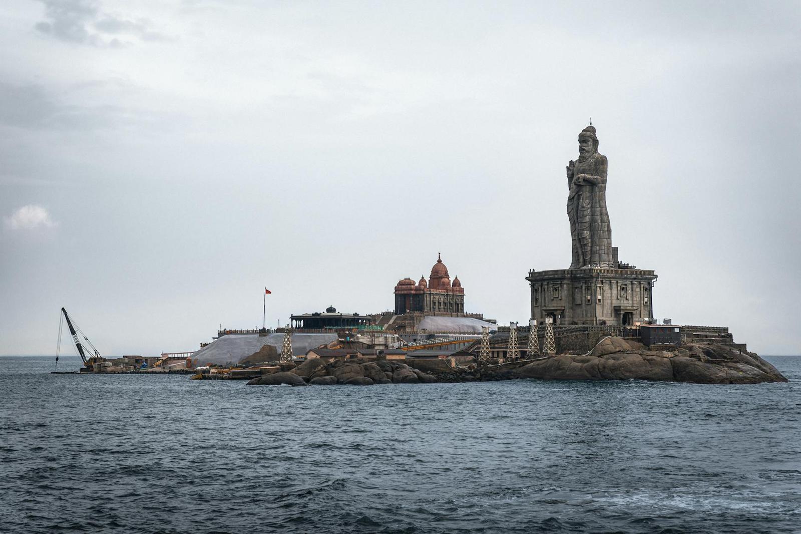 Large stone statue rising from a rocky island memorial in the sea