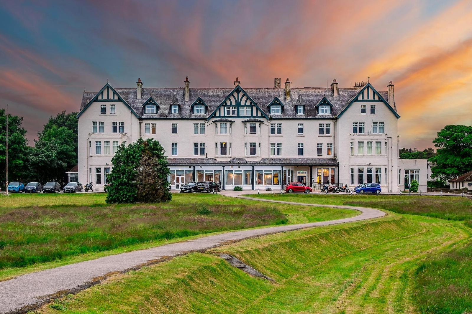 A grand heritage hotel building at sunset with lawn and driveway