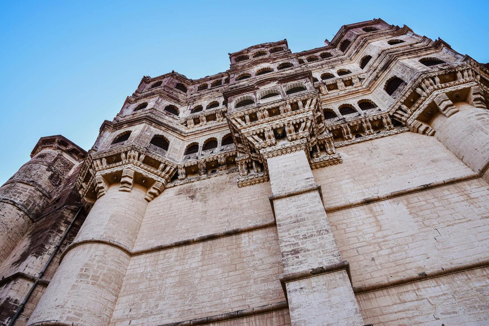 Low-angle view of Mehrangarh Fort showcasing intricate architecture against a clear blue sky