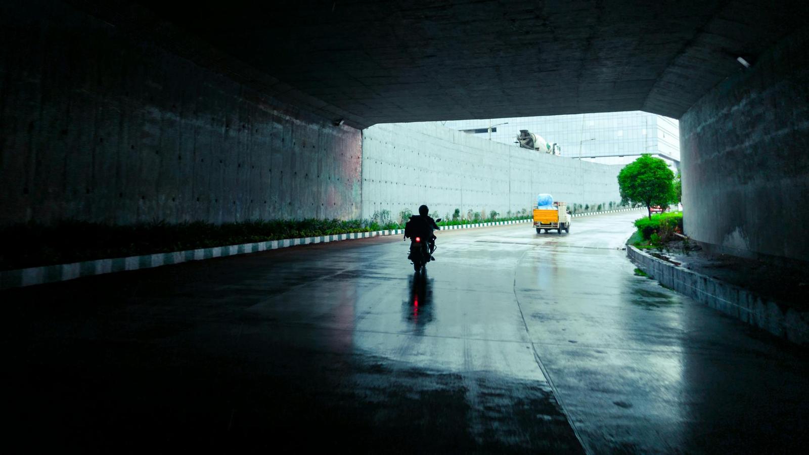 A motorcyclist riding through a wet underpass in the rain
