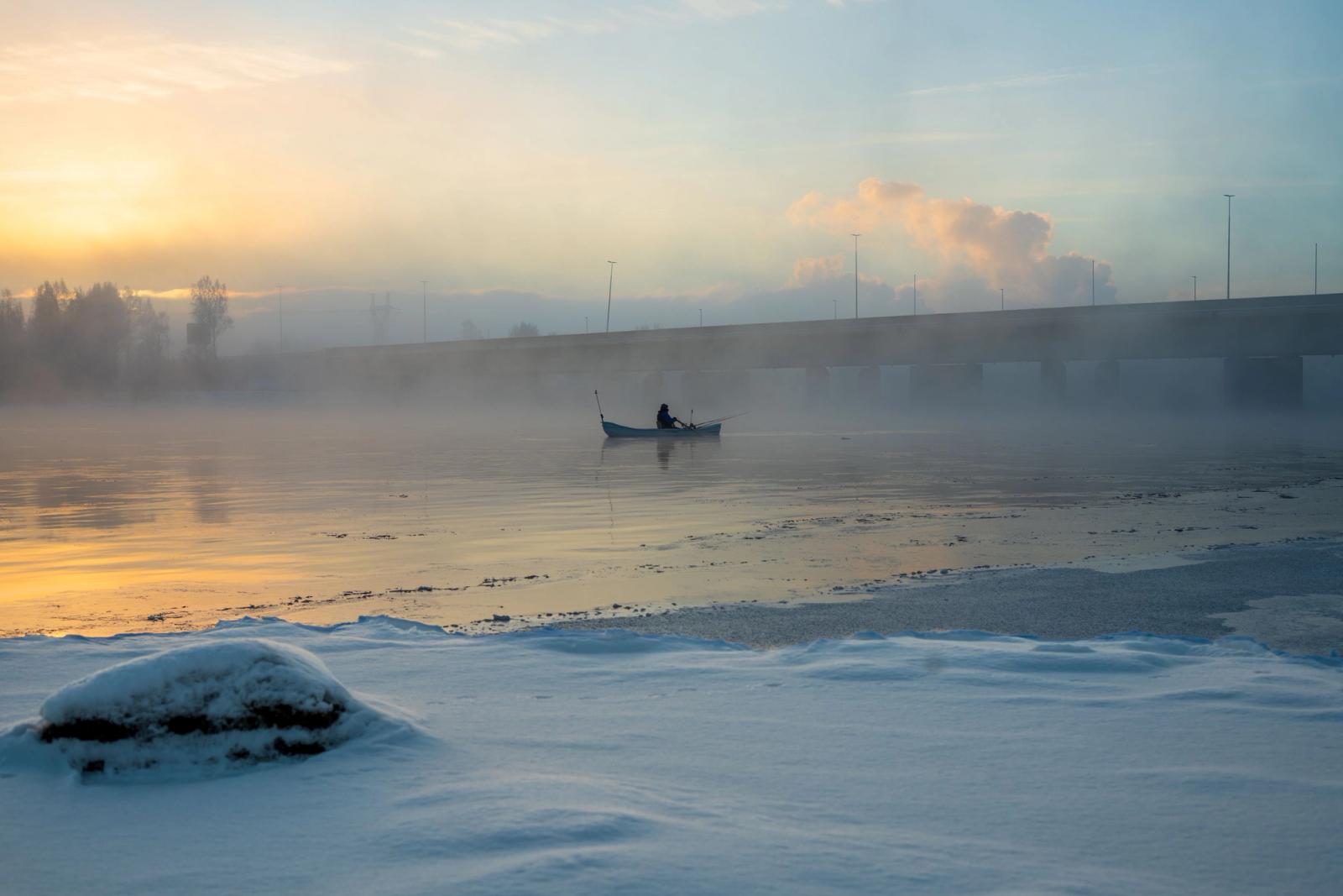 Solitary boatman on a misty river at sunset in Keminmaa, Finland, surrounded by snow