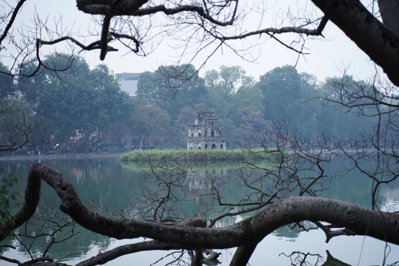Peaceful view of Turtle Tower in Hanoi framed by branches over serene Hoàn Kiếm Lake