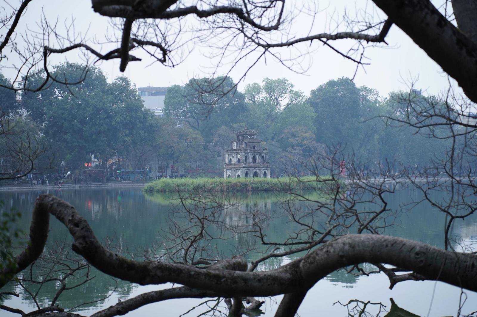 Peaceful view of Turtle Tower in Hanoi framed by branches over serene Hoàn Kiếm Lake