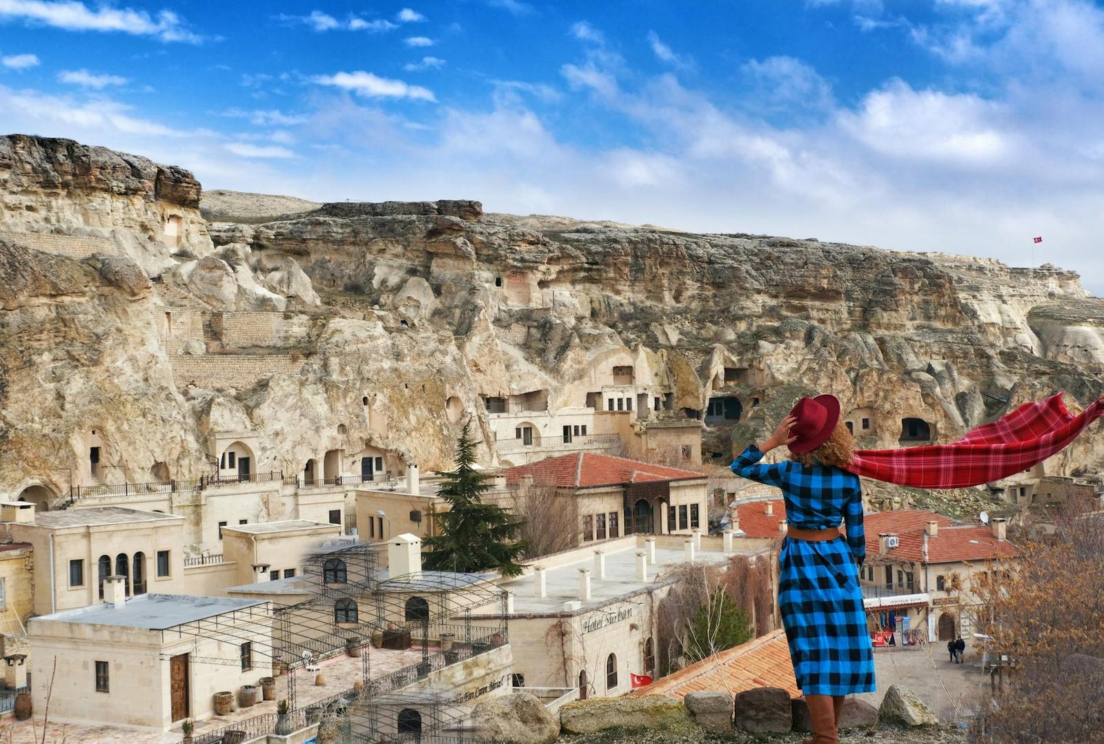 A woman in a blue dress with a red scarf overlooking a cliffside cave town