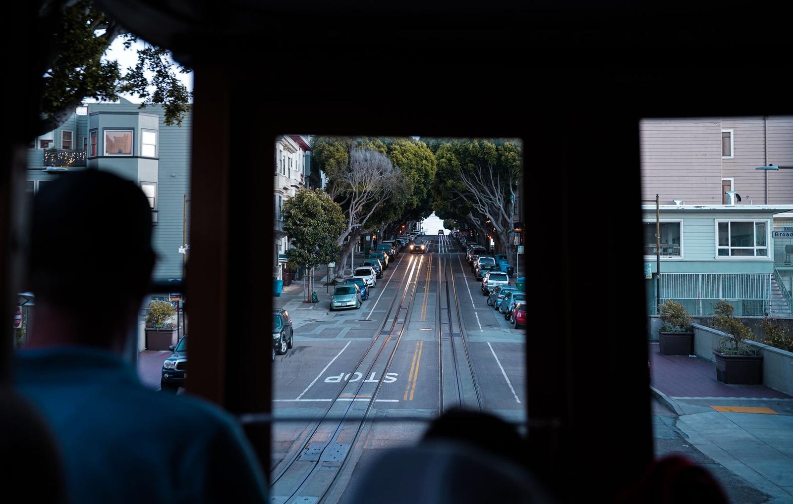 Looking out a cable car window down a tree-lined street with passengers silhouetted in the frame