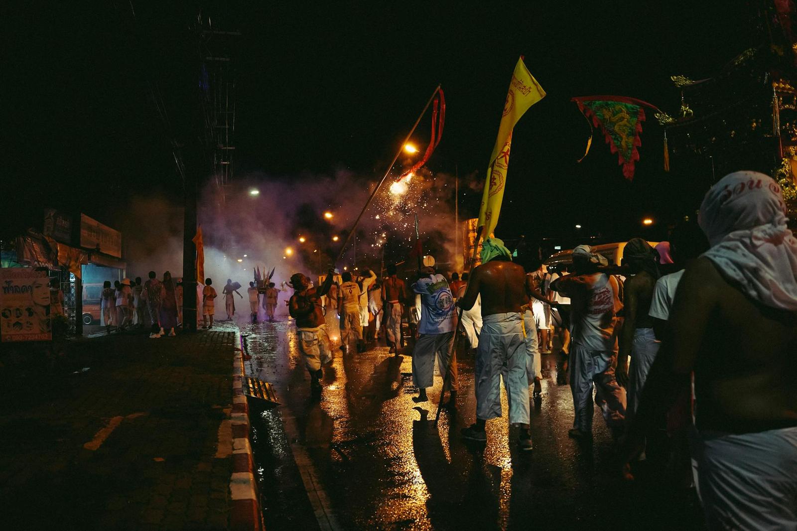 A night street procession with people carrying flags through smoke and lantern light