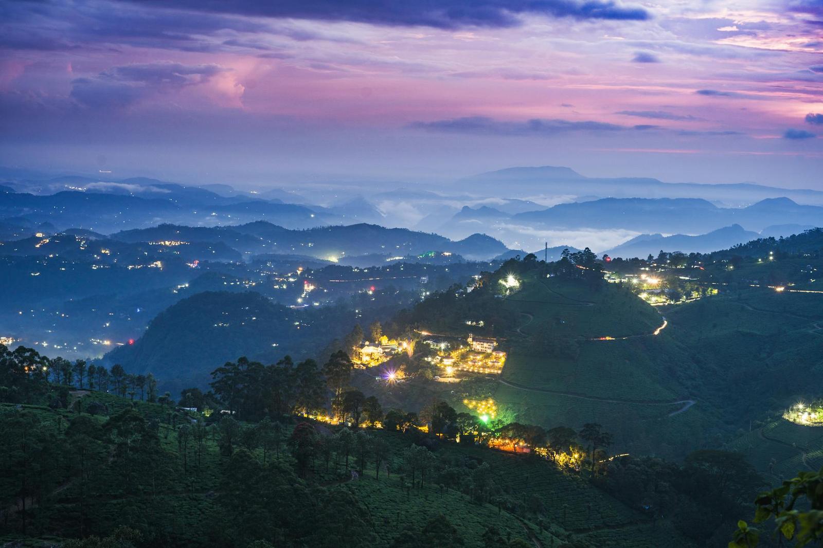 Lights of a hillside settlement glowing at dusk across misty valleys