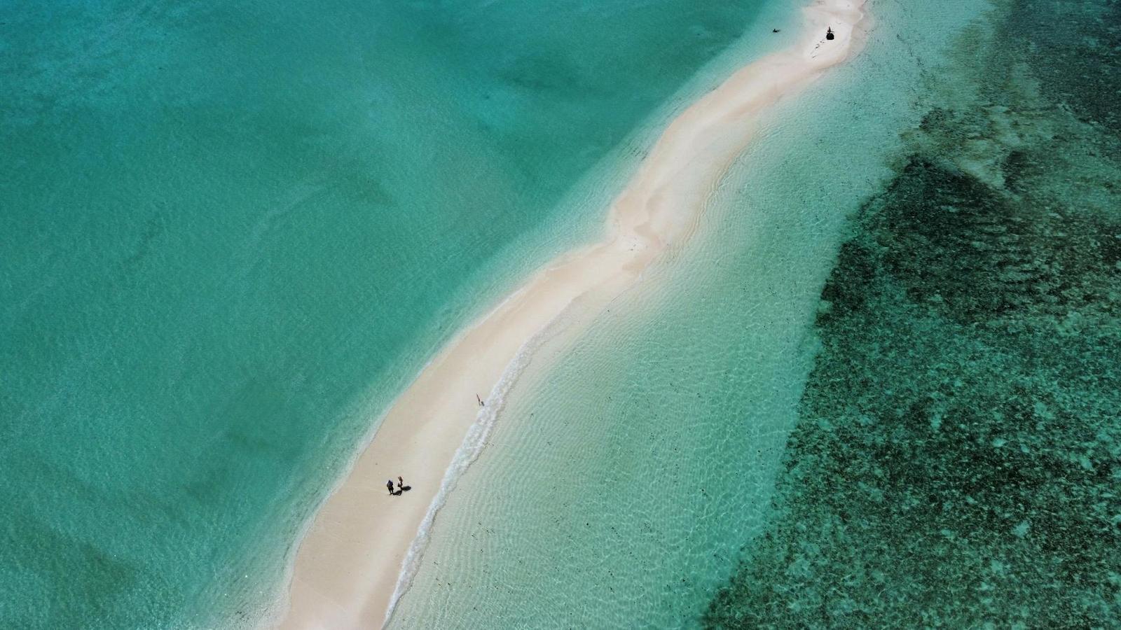Aerial view of a narrow sandbar between two shades of turquoise water