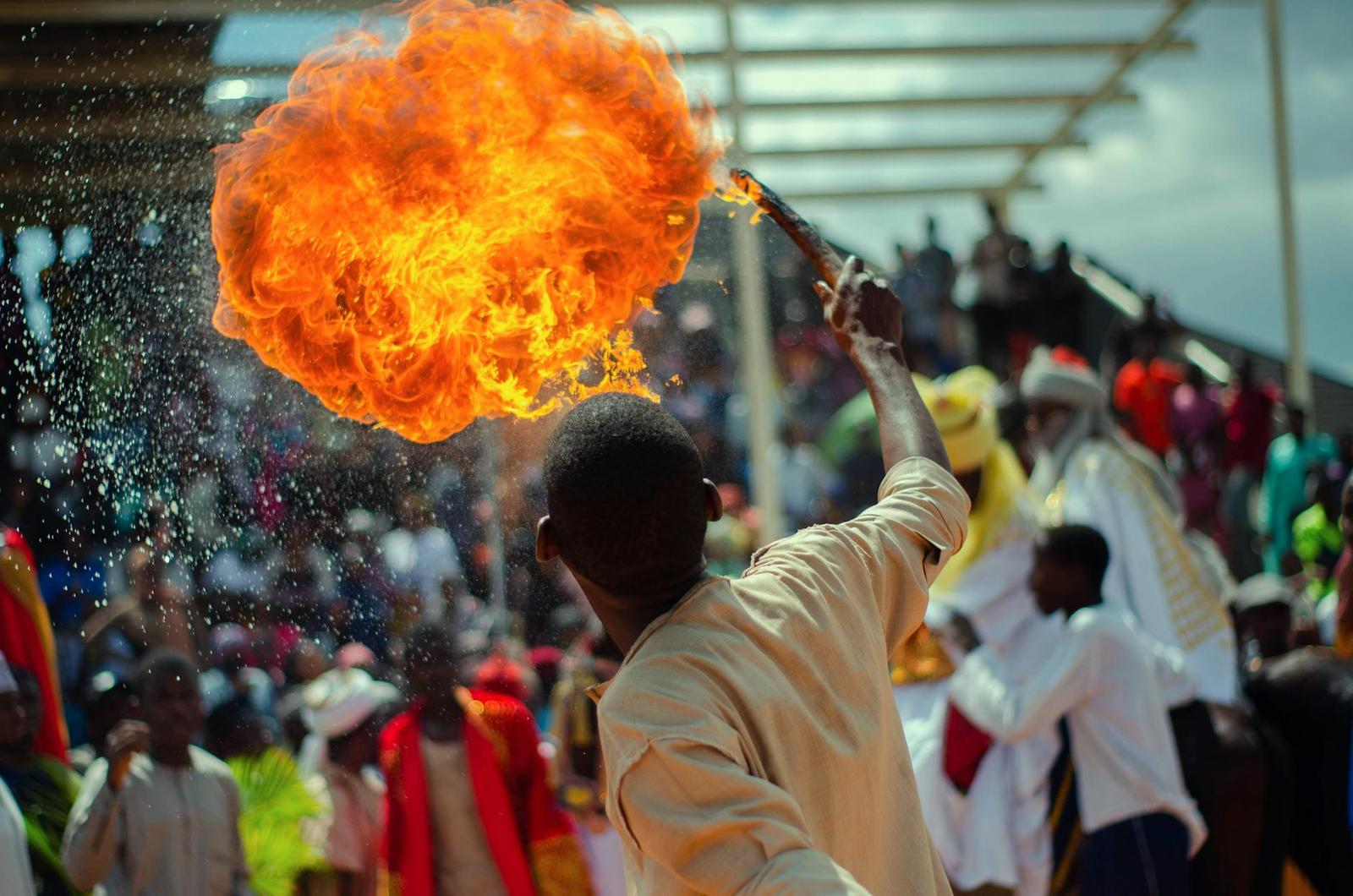 A performer hurls a burst of fire above a crowd at an outdoor festival