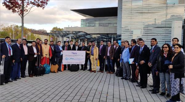 Delegation posing with a banner outside a modern glass building.