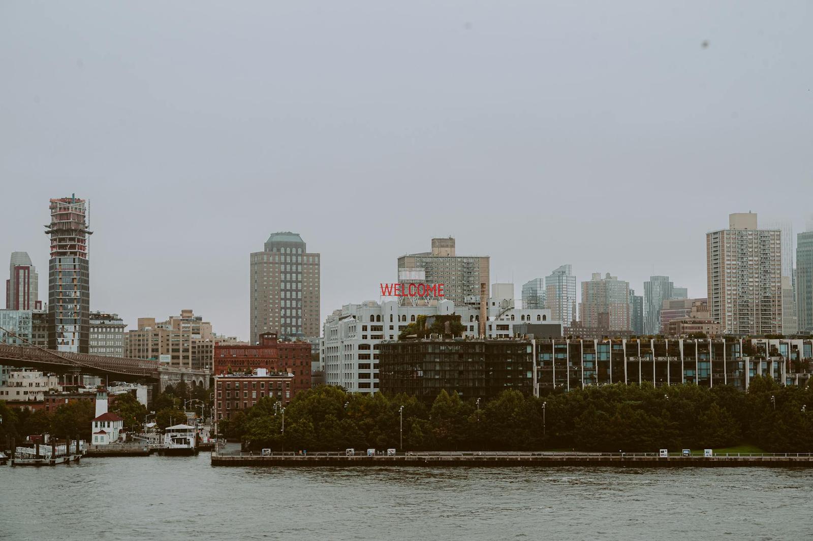 A hazy waterfront skyline with a lit welcome sign among the buildings