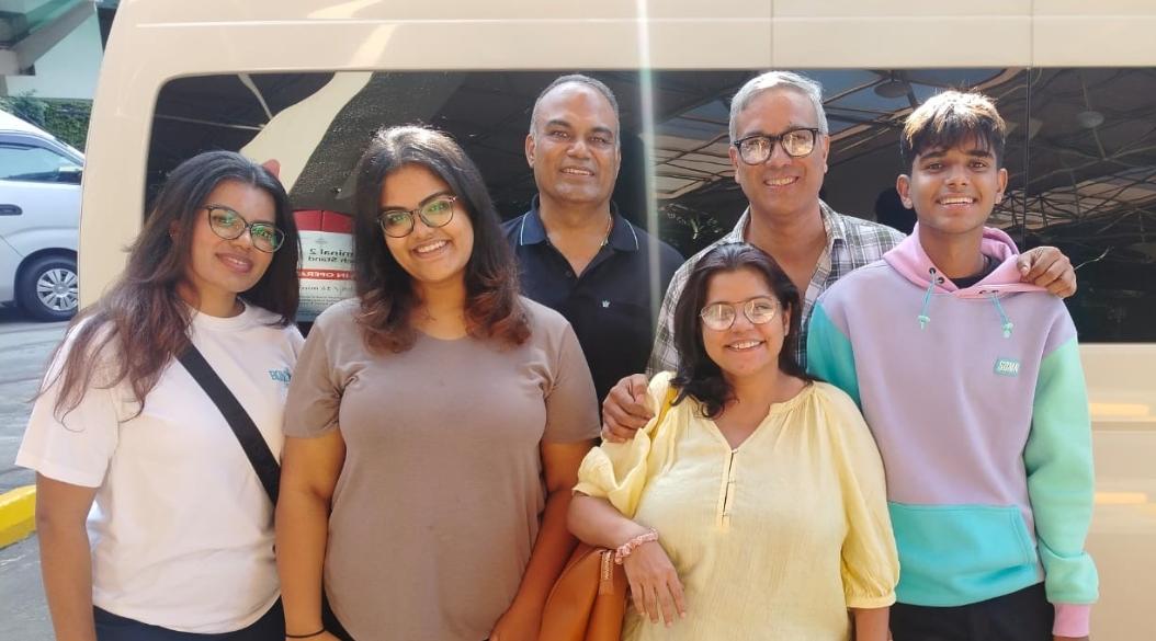 A group of six people posing together in front of a white vehicle