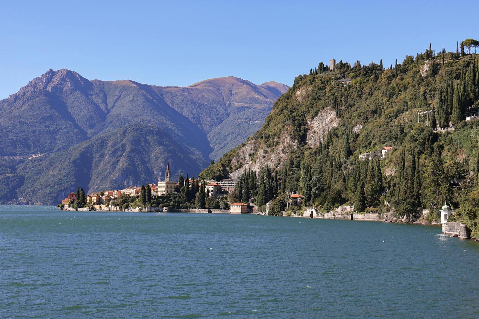 Lakeside village nestled beneath forested mountains with cypress trees