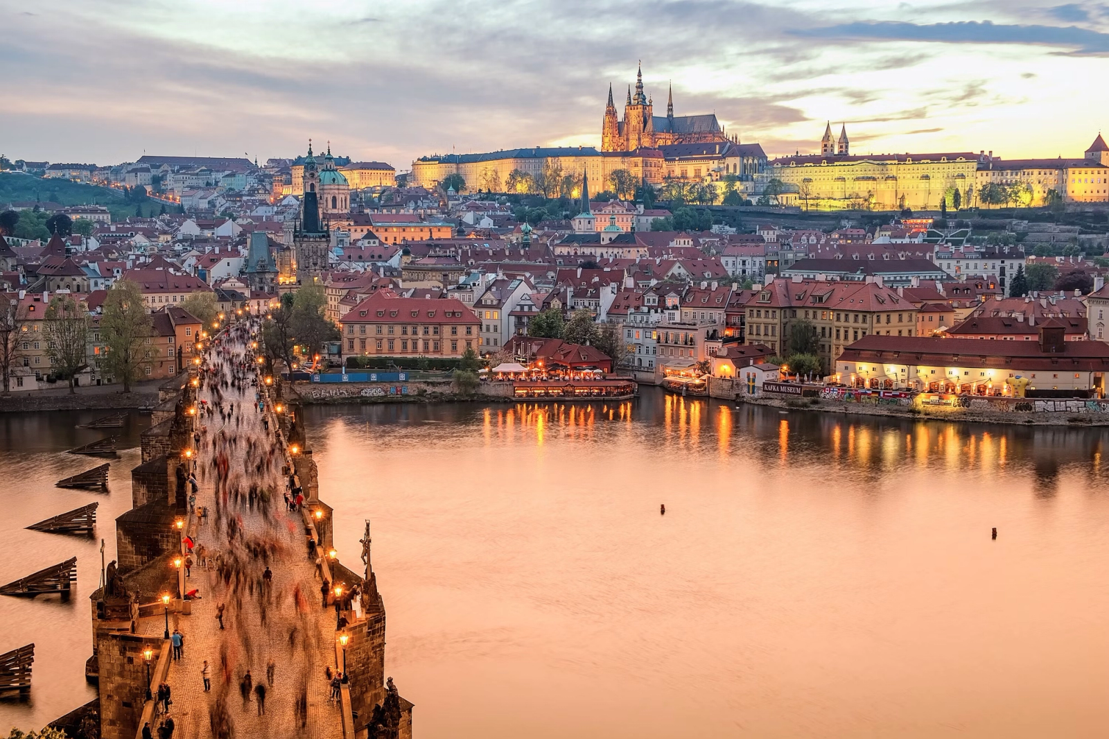 Prague Castle glowing above the Vltava River and Charles Bridge at dusk