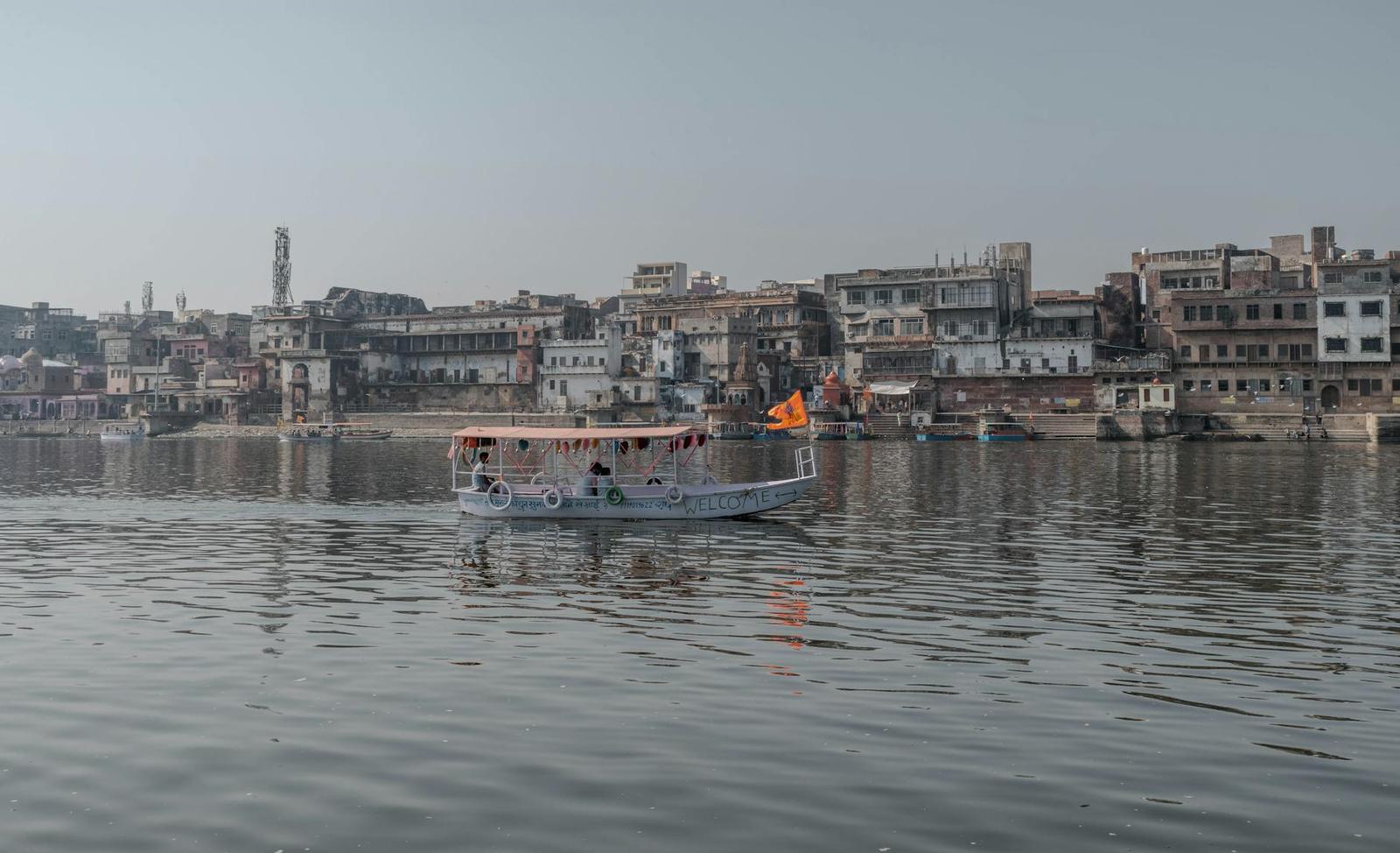 Flag-draped river boat drifting past a hazy riverside townscape