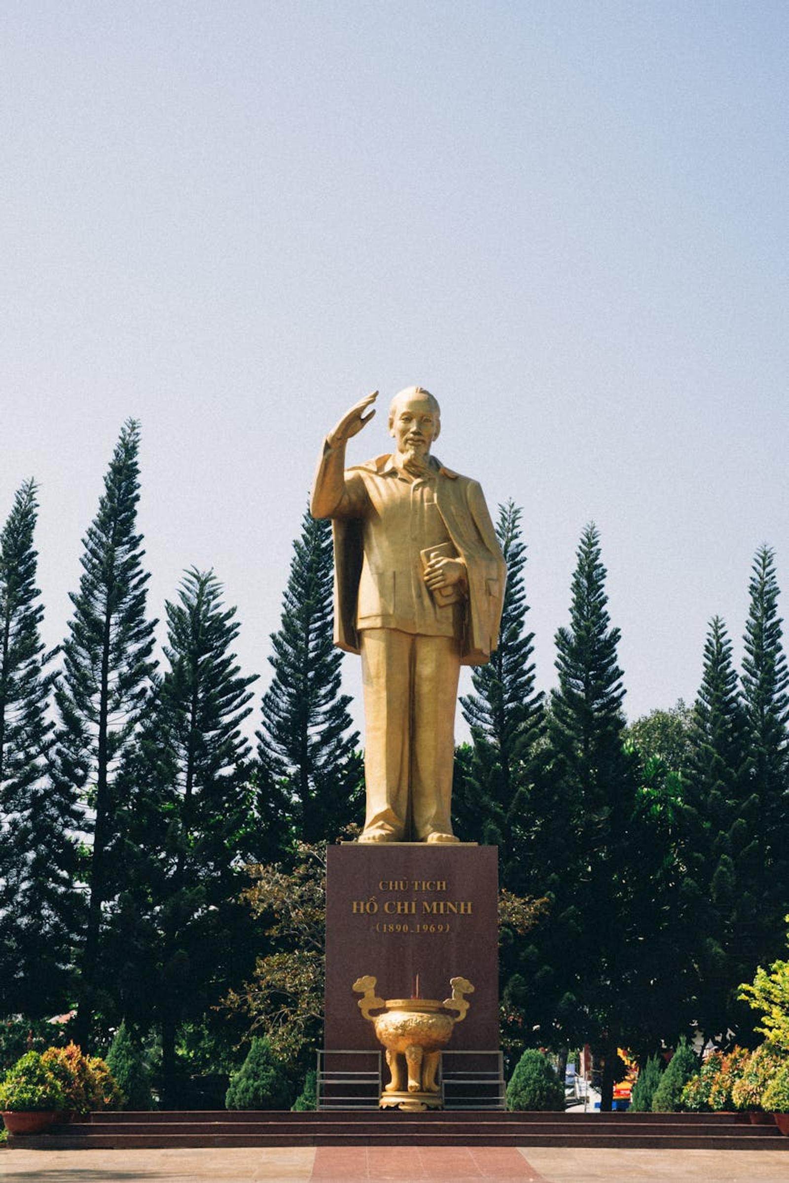 Golden statue of a saluting historic leader among tall pine trees