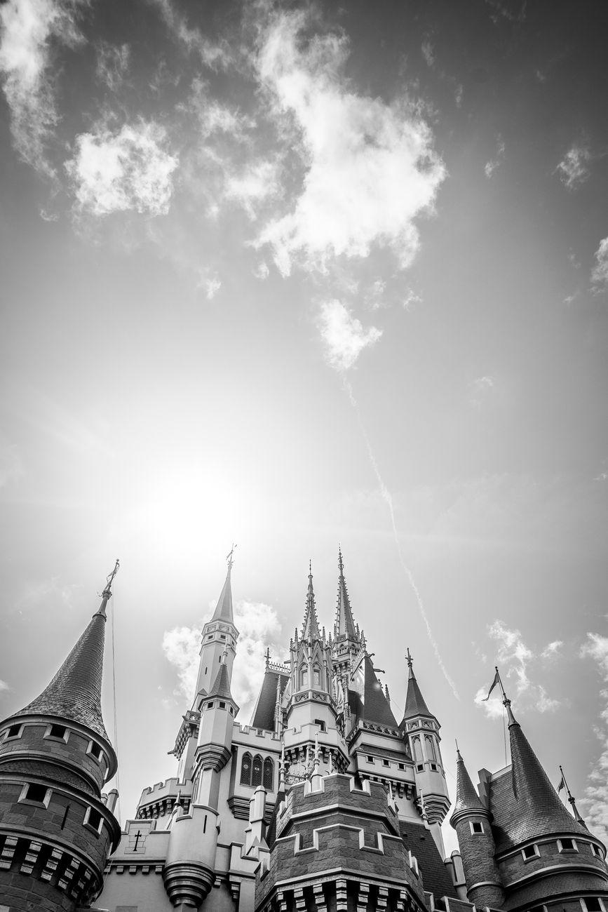 Black and white view of castle spires glowing against sun-flared clouds