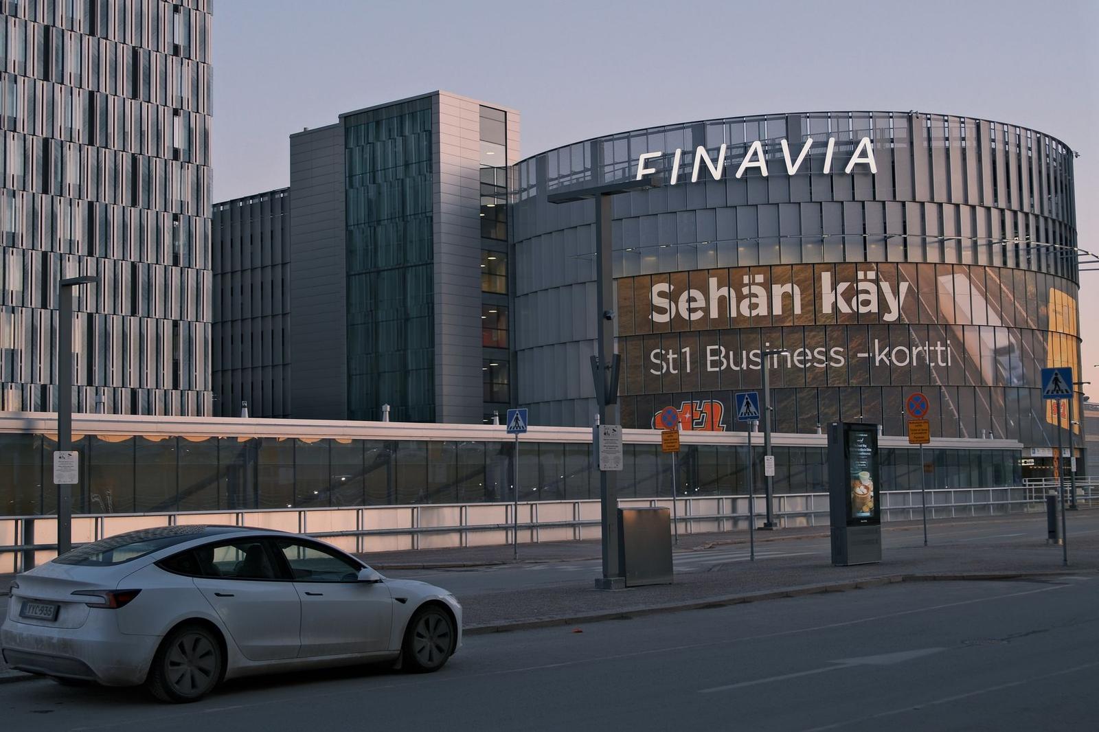 Modern glass airport terminal with a car parked outside at dusk