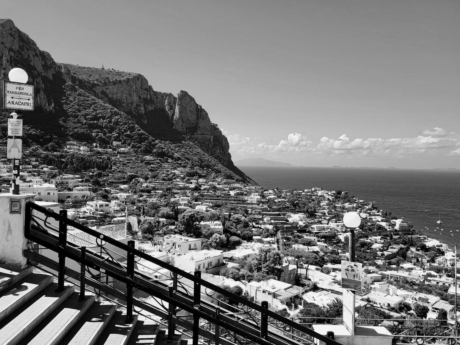 Black and white view of a hillside town beneath steep cliffs and the sea