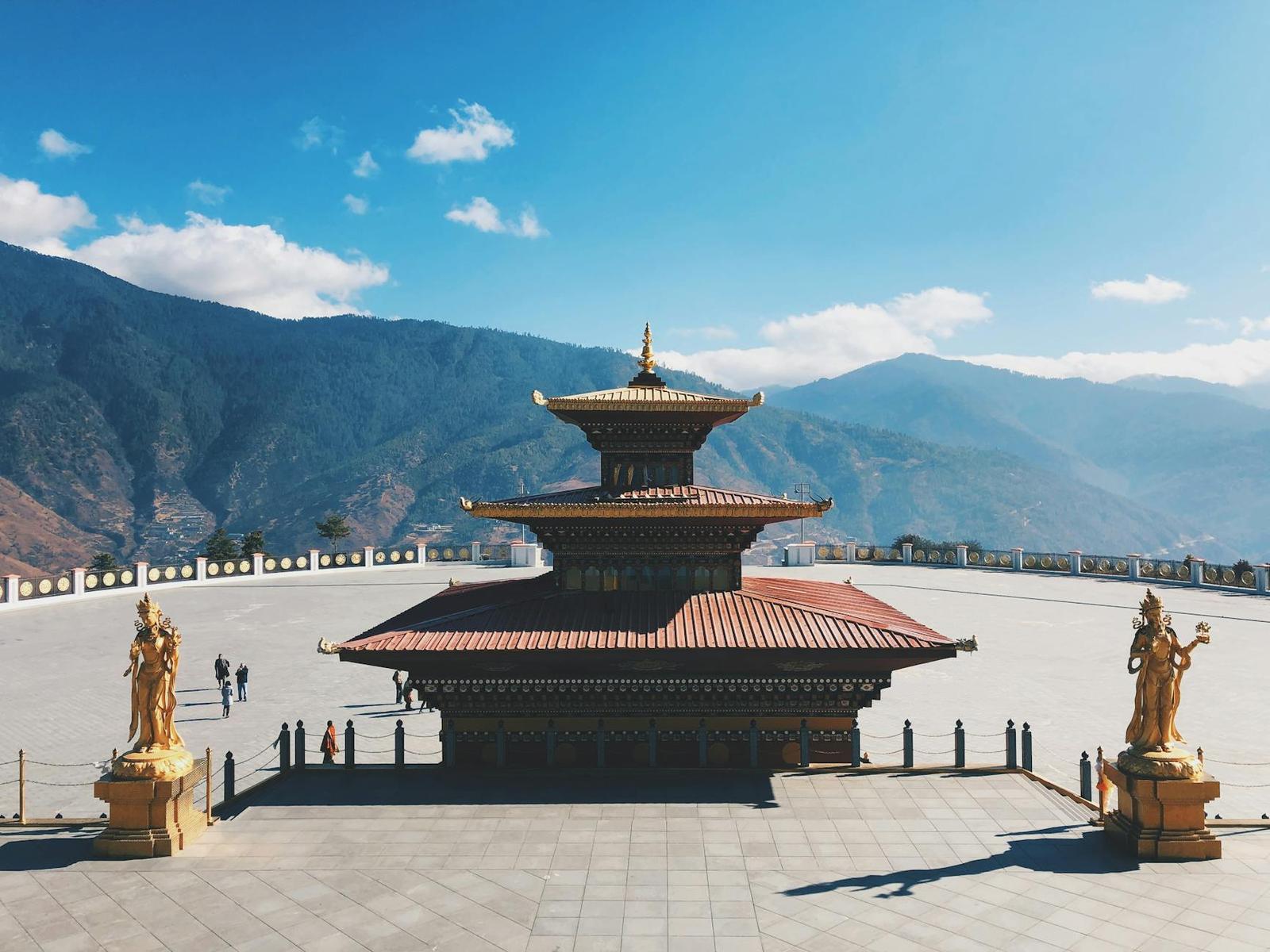 A tiered pagoda-style temple in a paved plaza flanked by golden statues