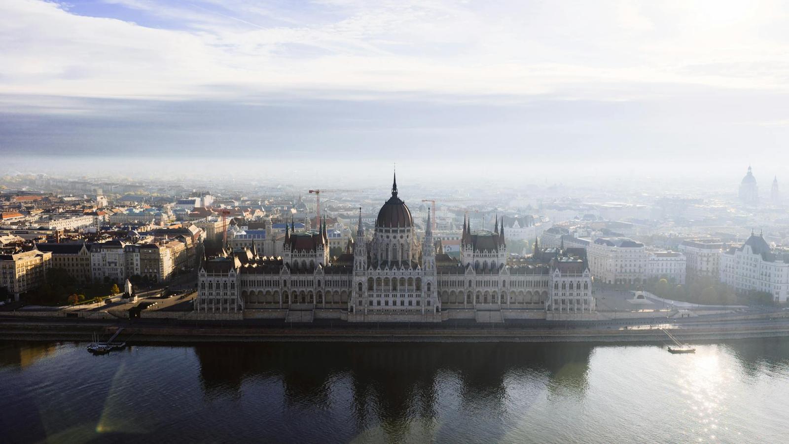 Aerial view of a grand riverside parliament building shrouded in haze