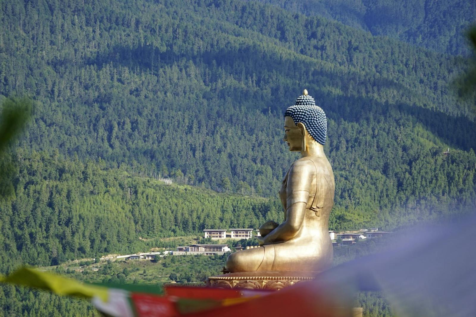 Buddha Dordenma statue amidst Bhutan's scenic mountains in Thimphu; a golden spiritual monument against dense forest