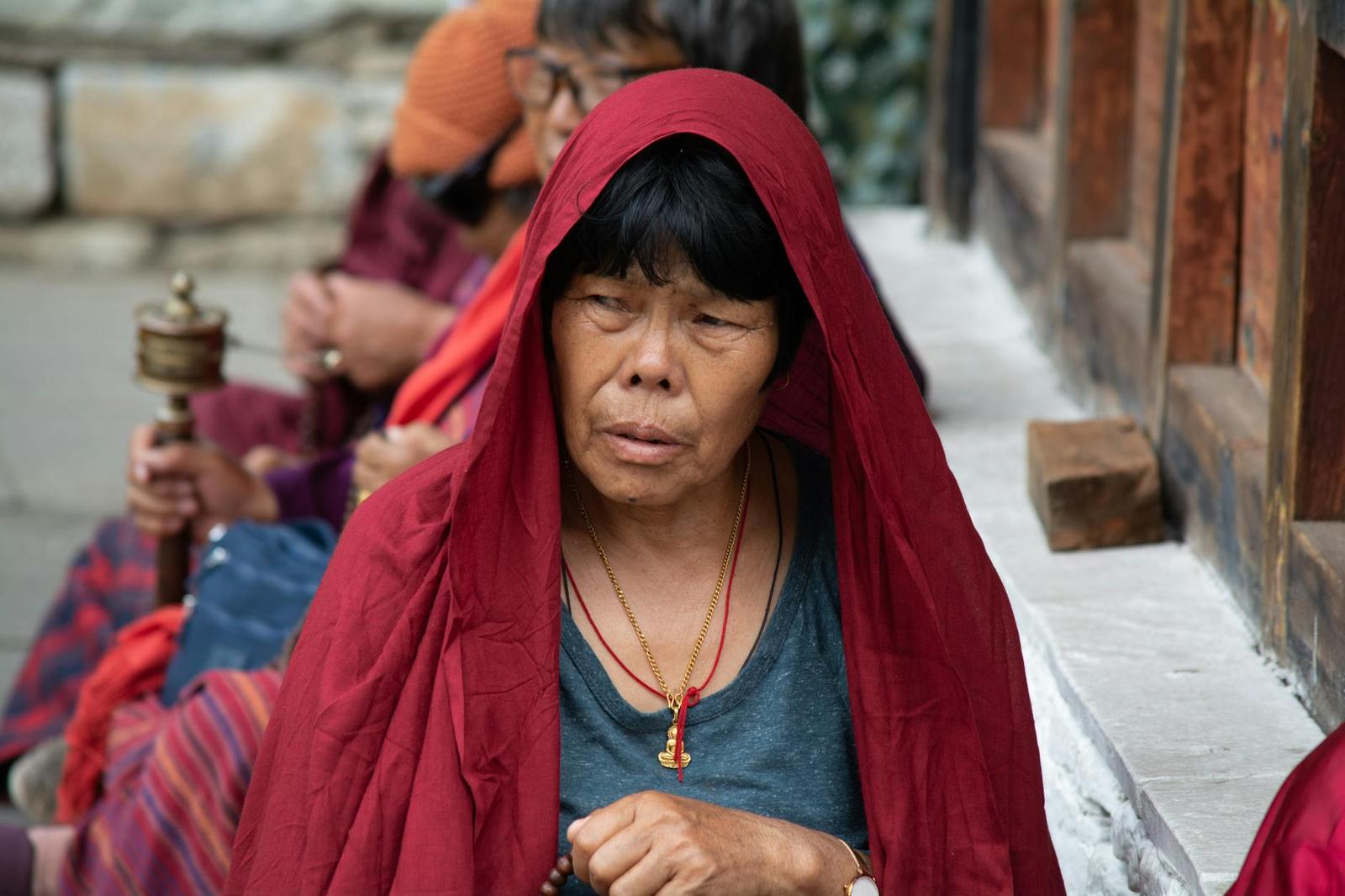 An elderly woman wrapped in a red shawl holding a prayer wheel