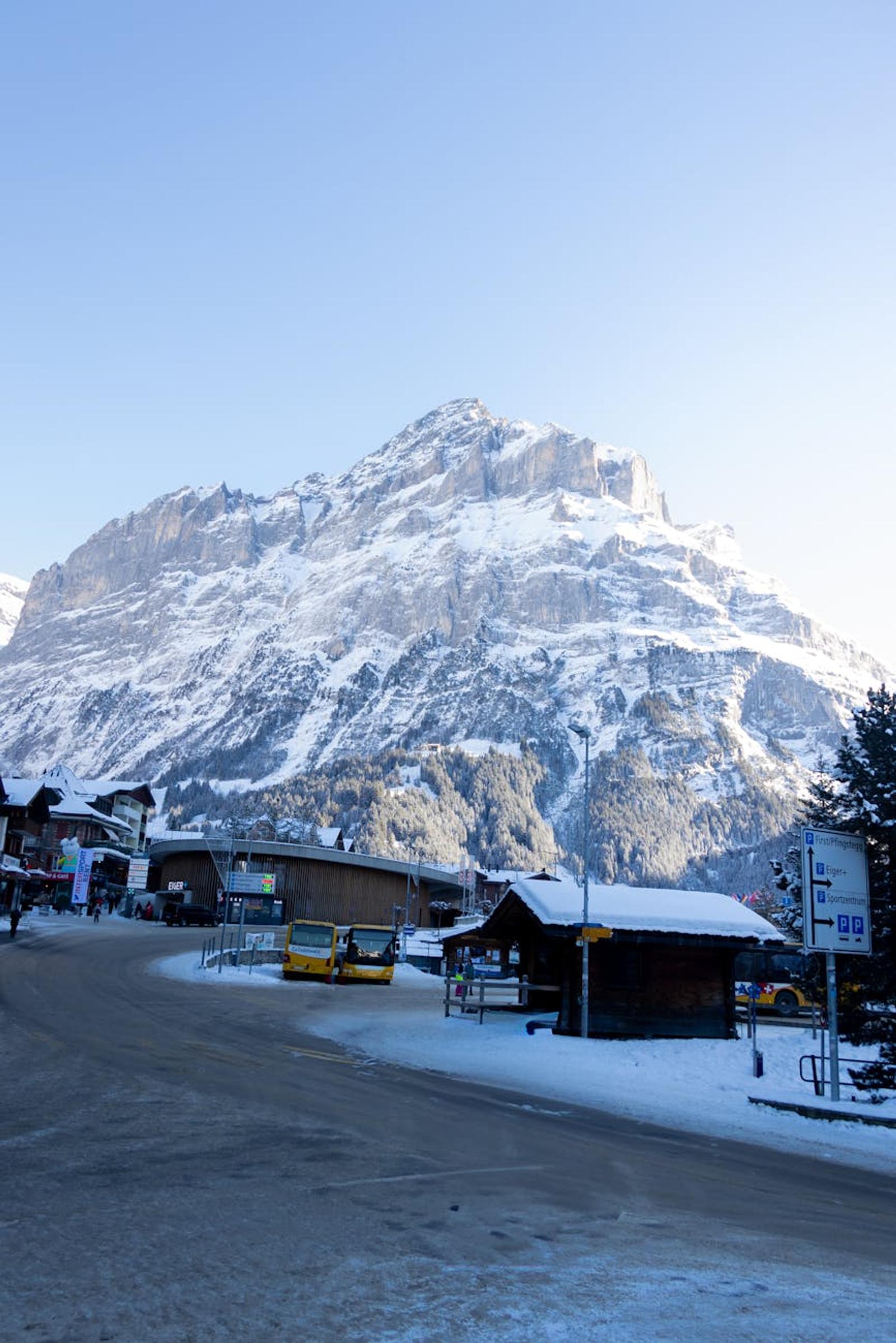 Snowy mountain village street with buses parked near a sheer peak