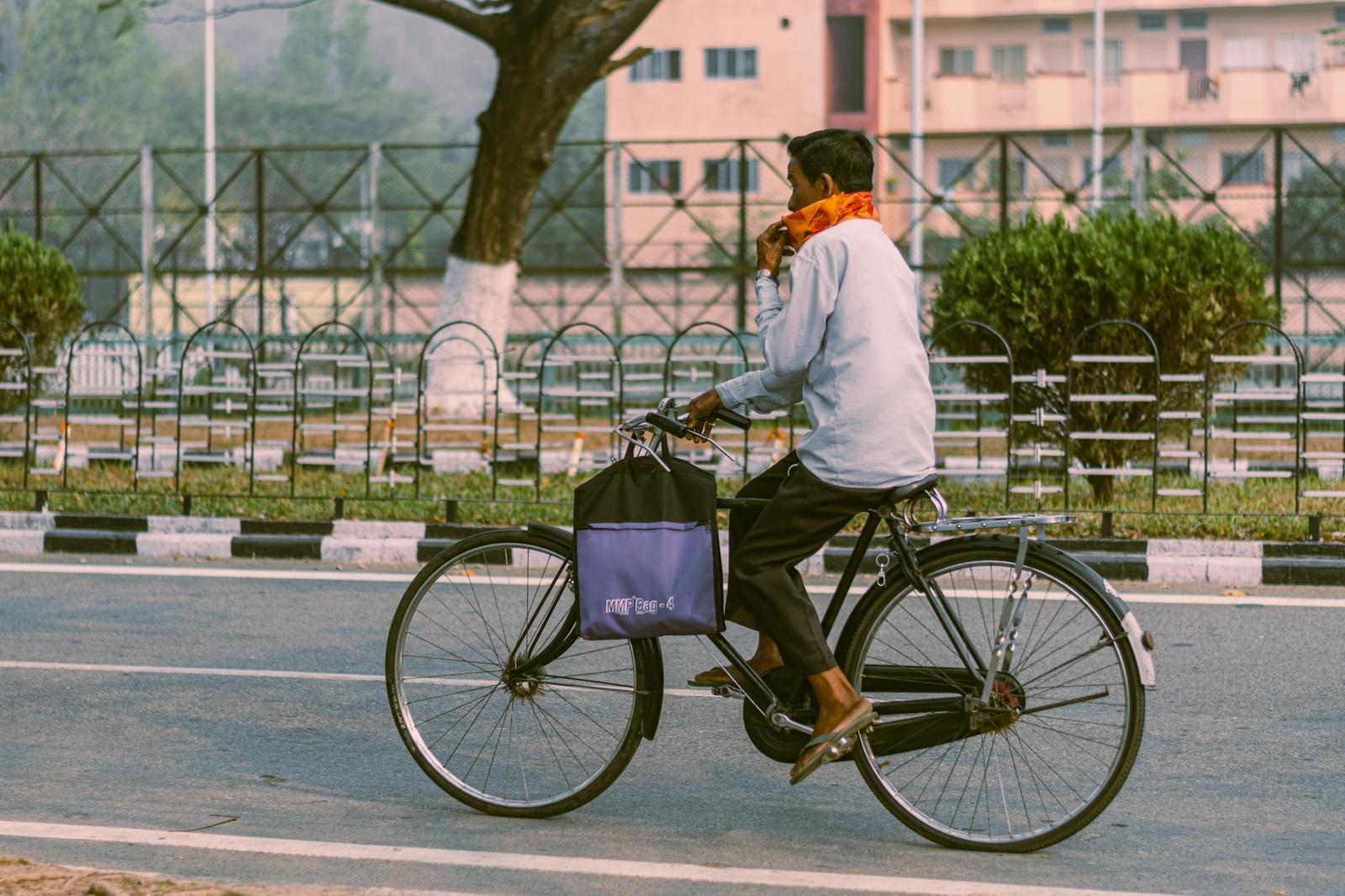 A man in an orange scarf cycles along a tree-lined street