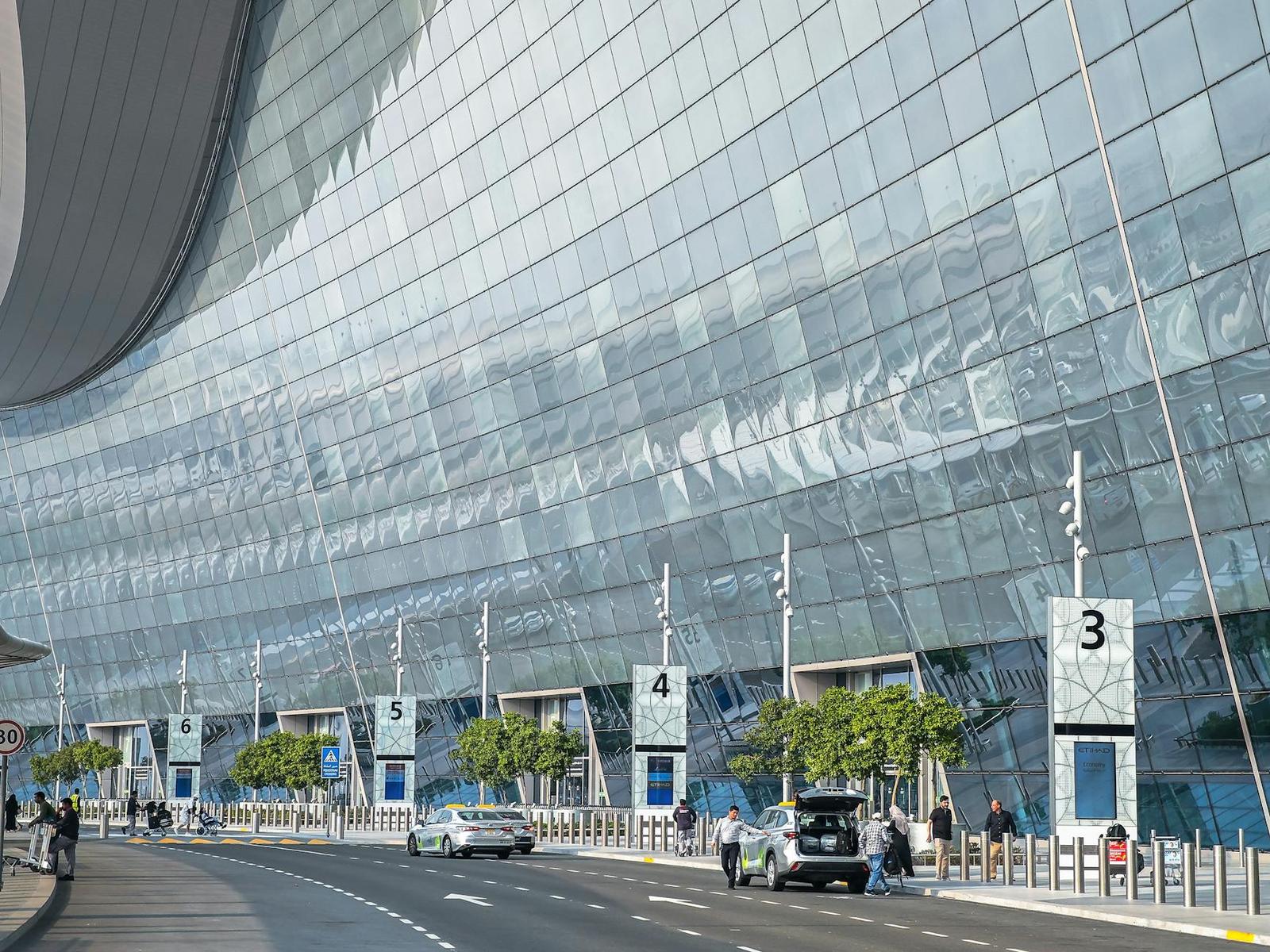 Curved glass facade of a modern airport terminal with numbered entrance pillars
