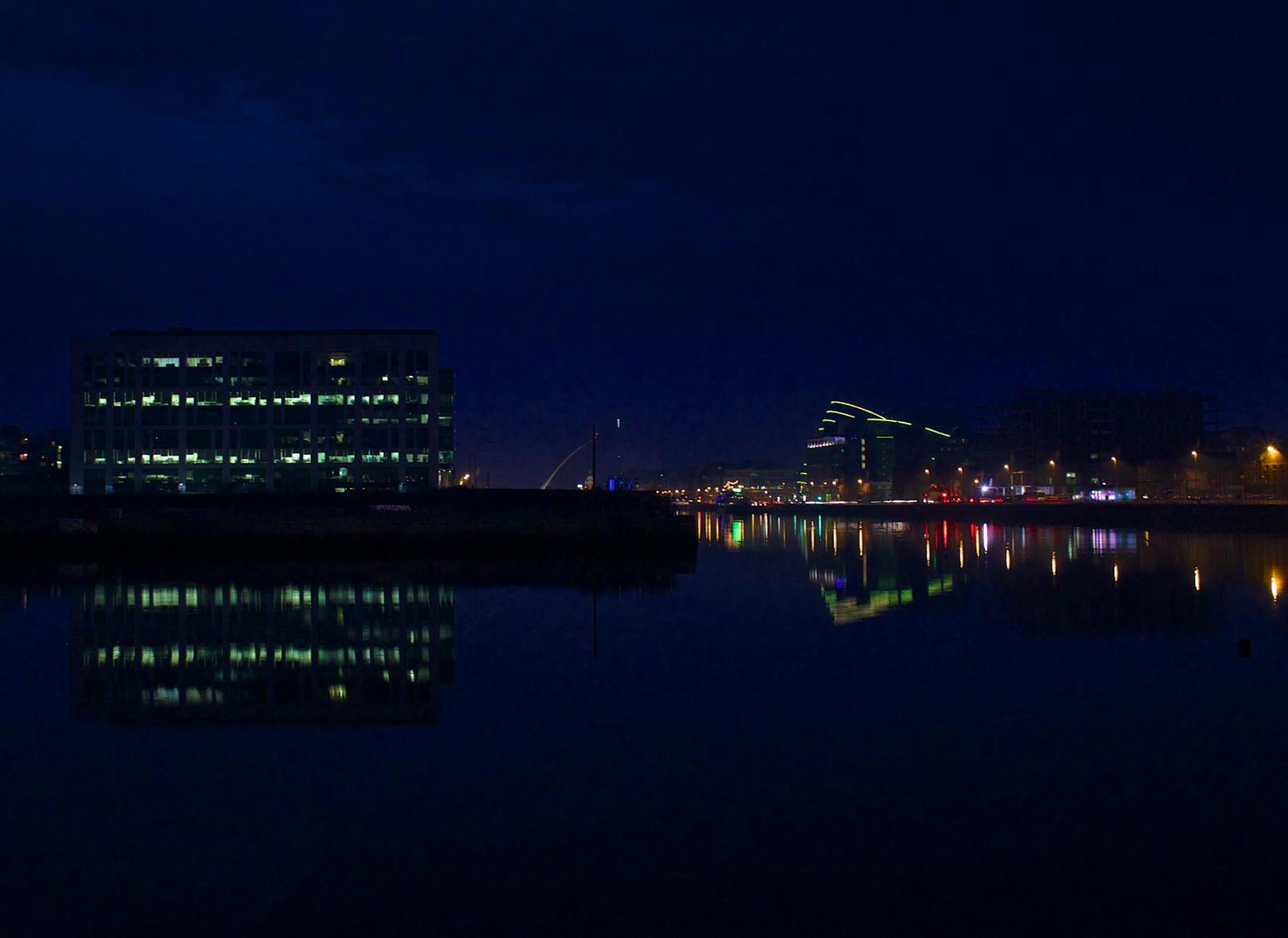 Office buildings reflected in a dark harbour at night