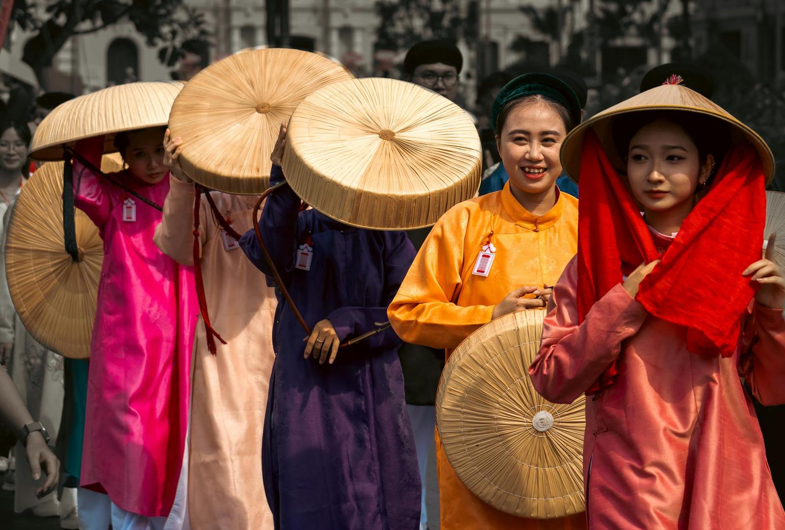 Group of women in colourful silk gowns holding wide woven hats at a street event