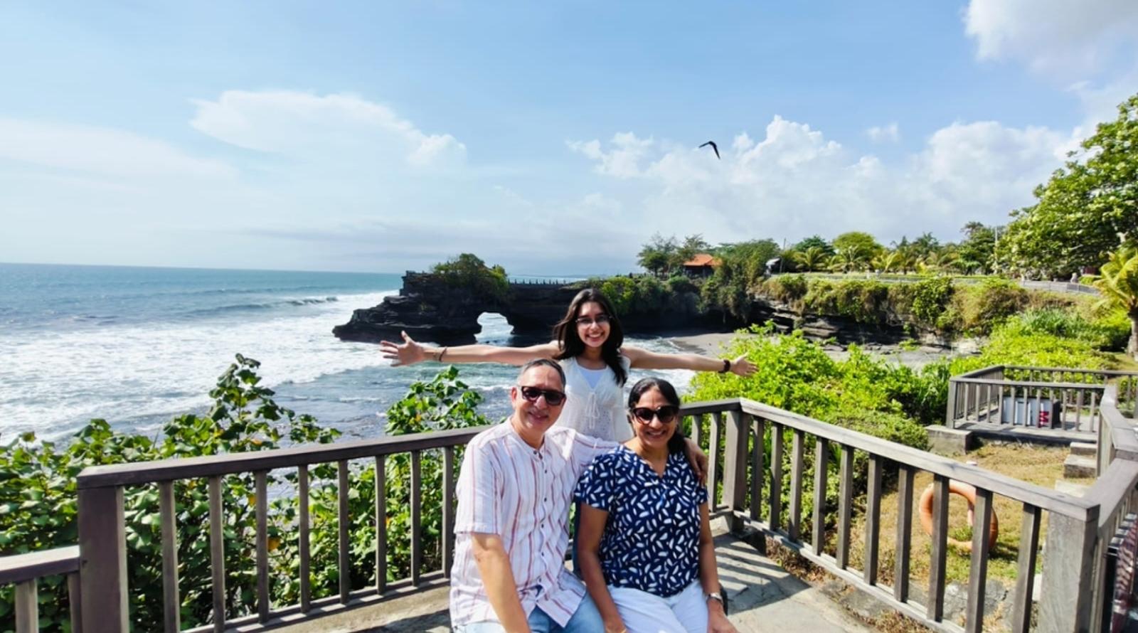 A family enjoys a scenic coastal view with smiles and open arms.