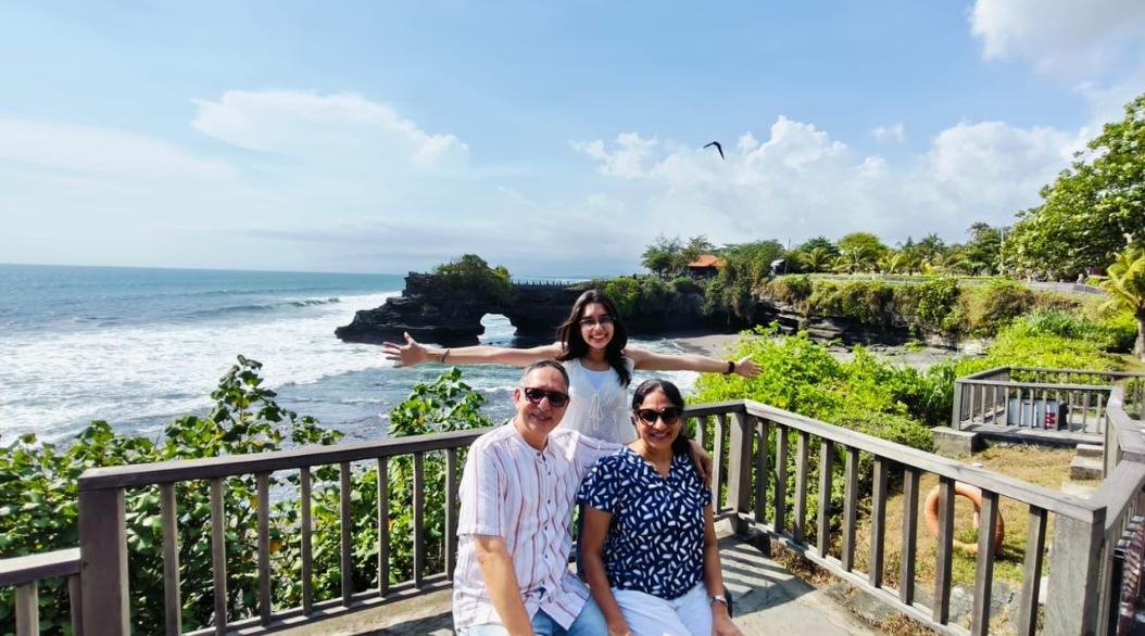 A family enjoys a scenic coastal view with smiles and open arms.