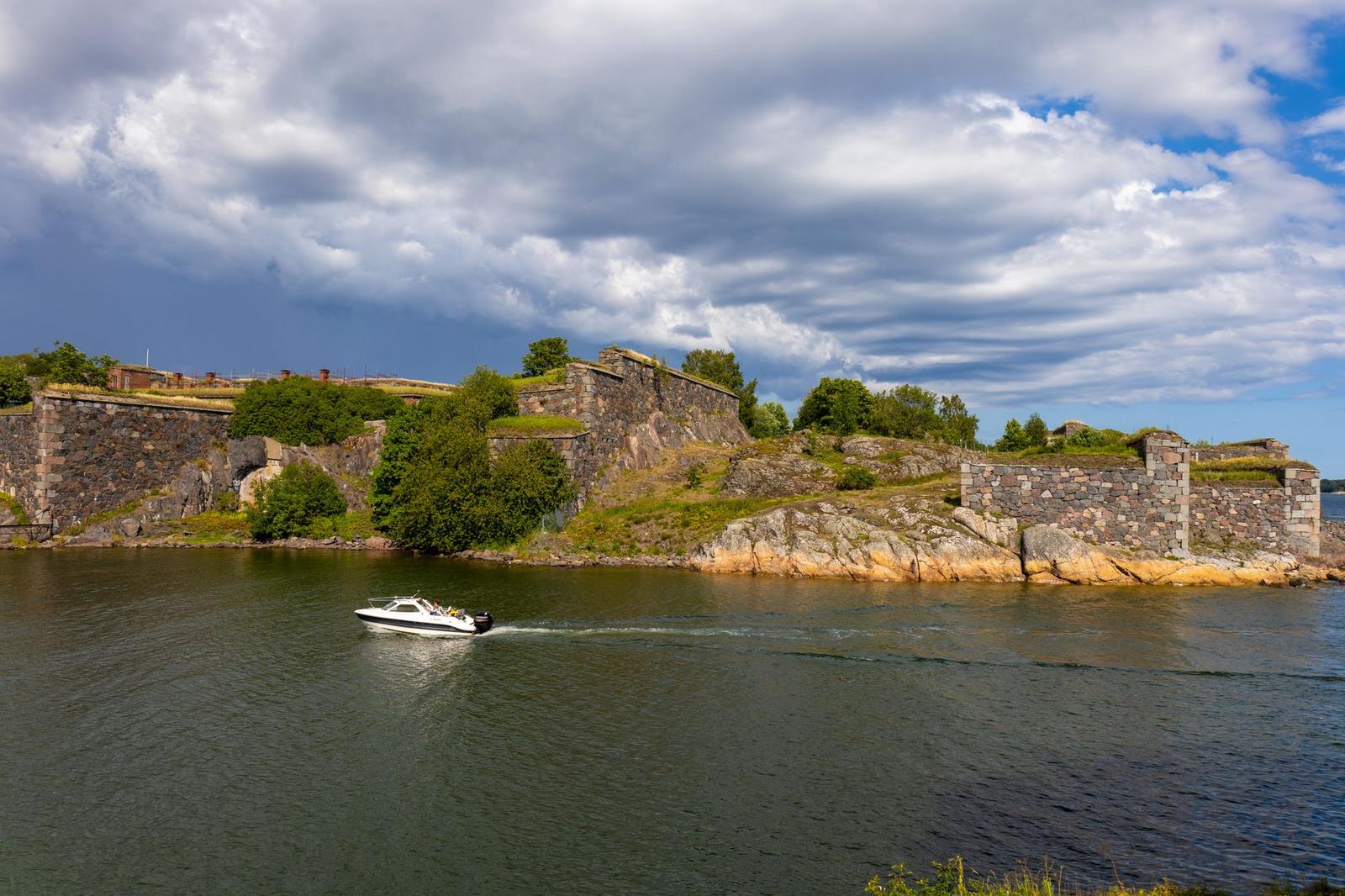 A scenic view of Suomenlinna Fortress with a boat passing by on a sunny day