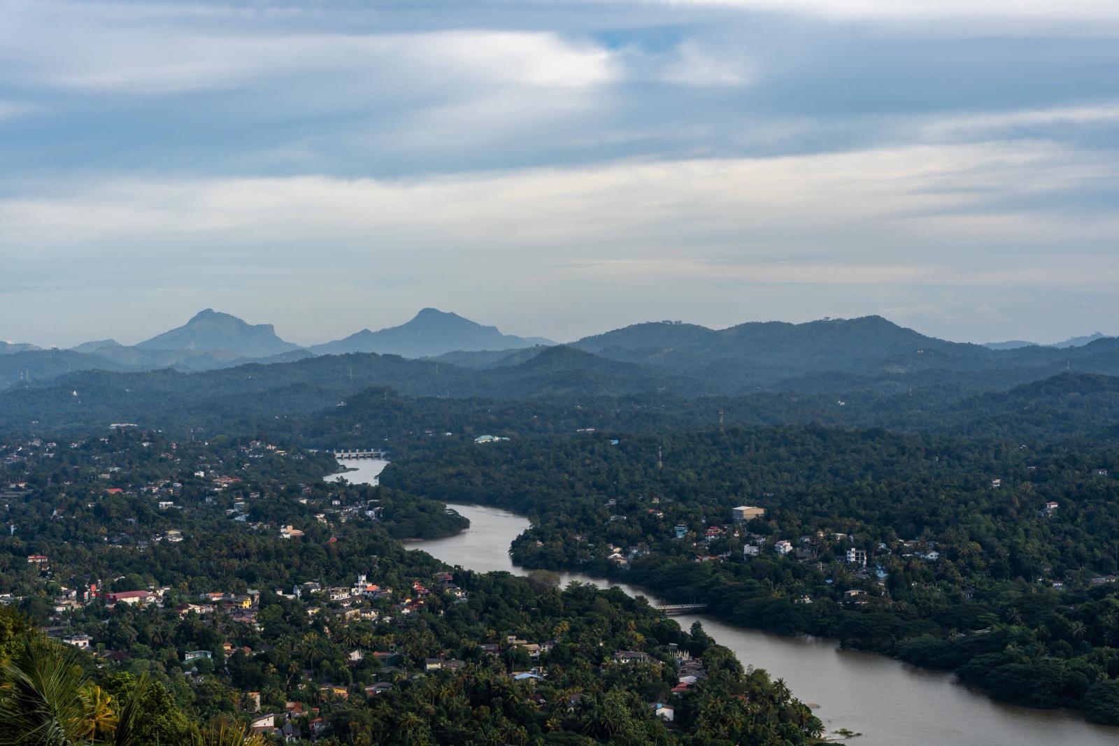 Aerial view of verdant hills, flowing river, and scattered houses under a partly cloudy sky