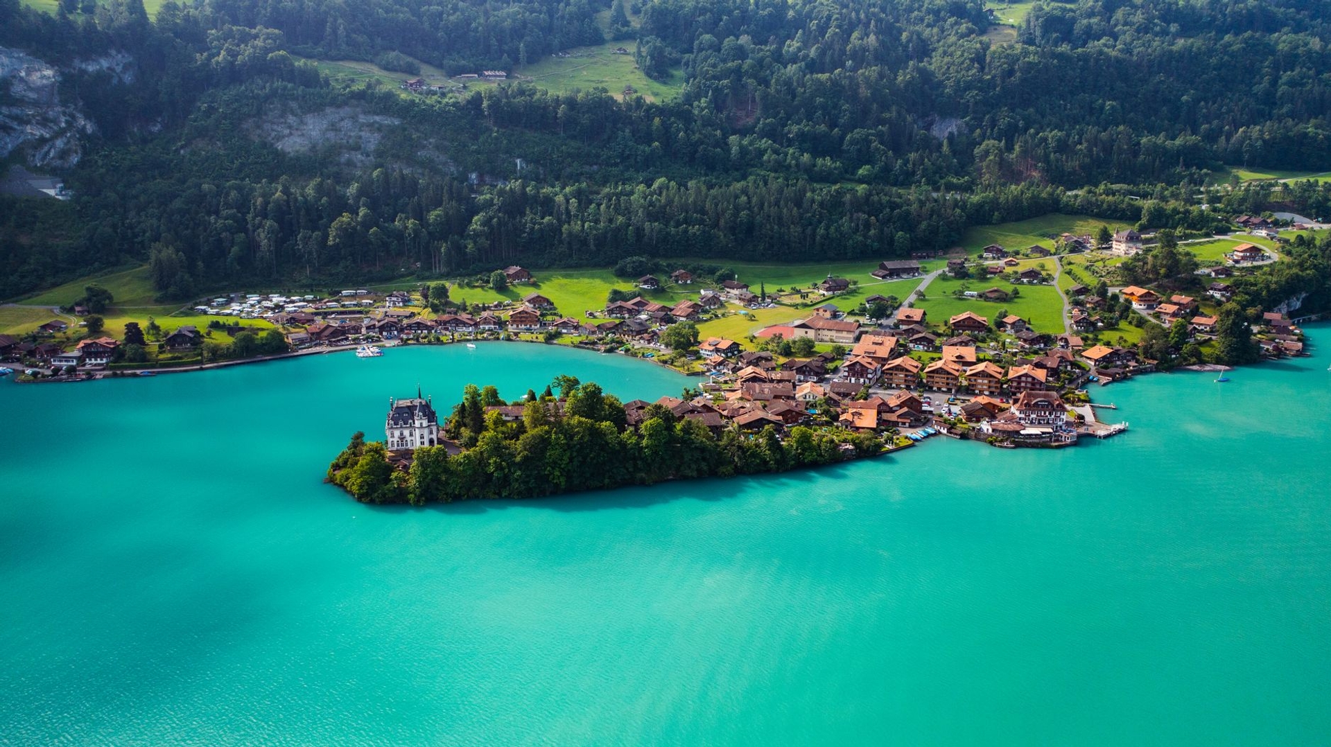 Aerial view of a turquoise lake curling around a wooded village peninsula