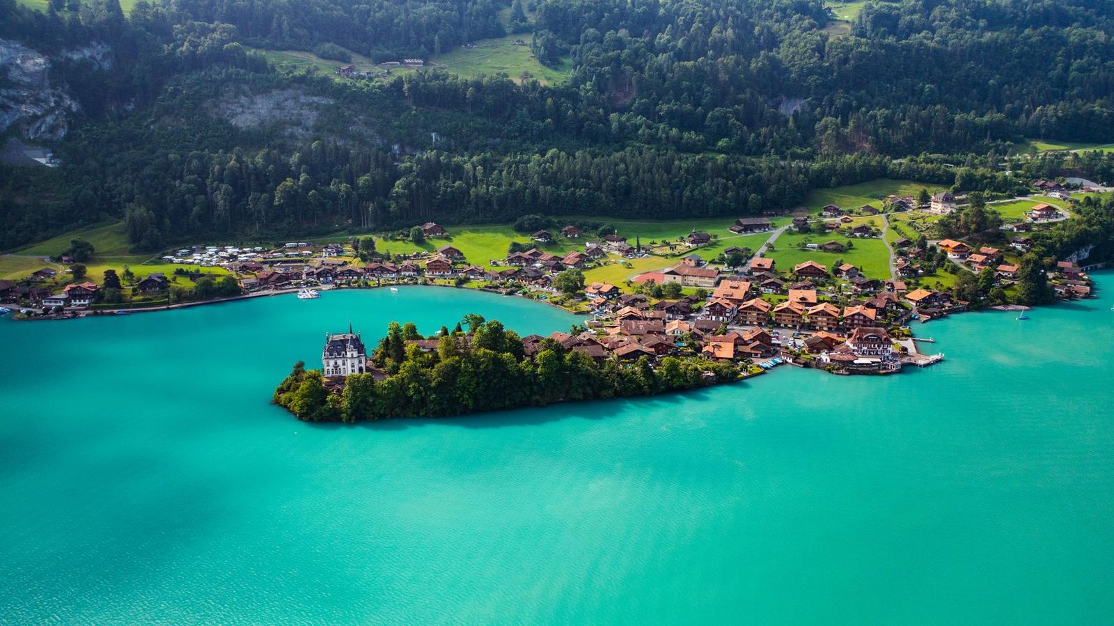 Aerial view of a turquoise lake curling around a wooded village peninsula