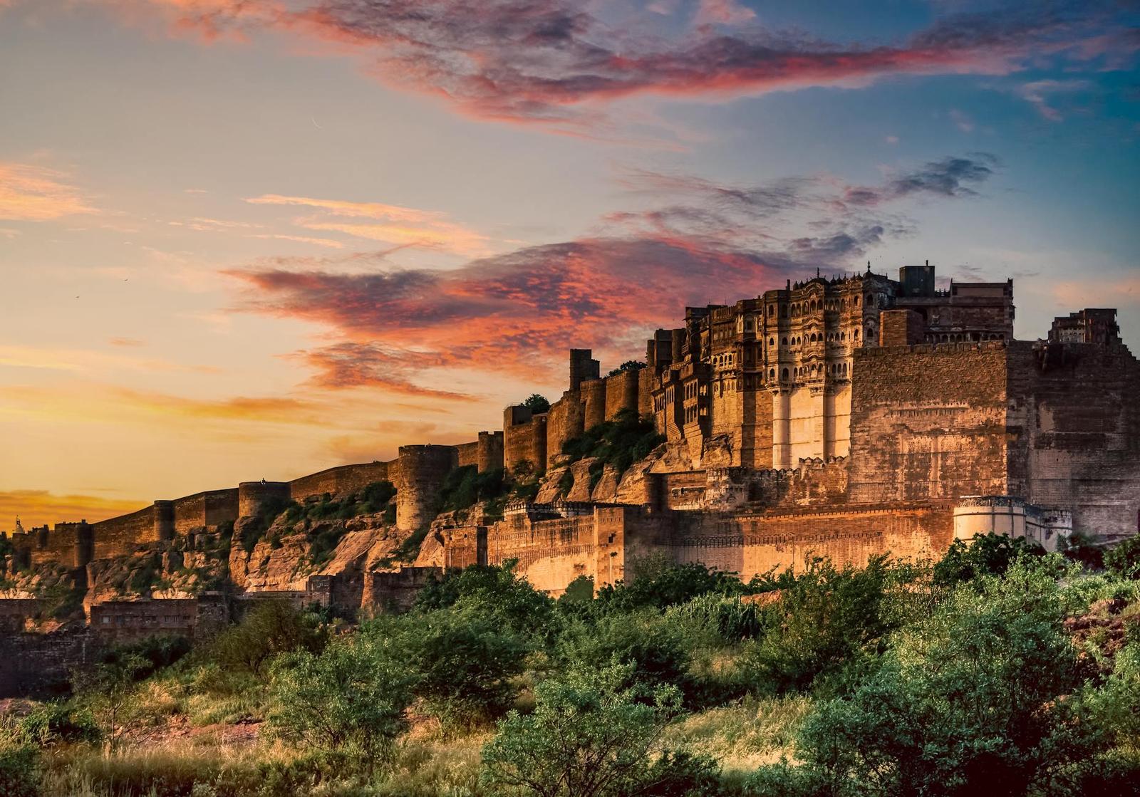A massive hilltop fort wall glowing under a fiery sunset sky