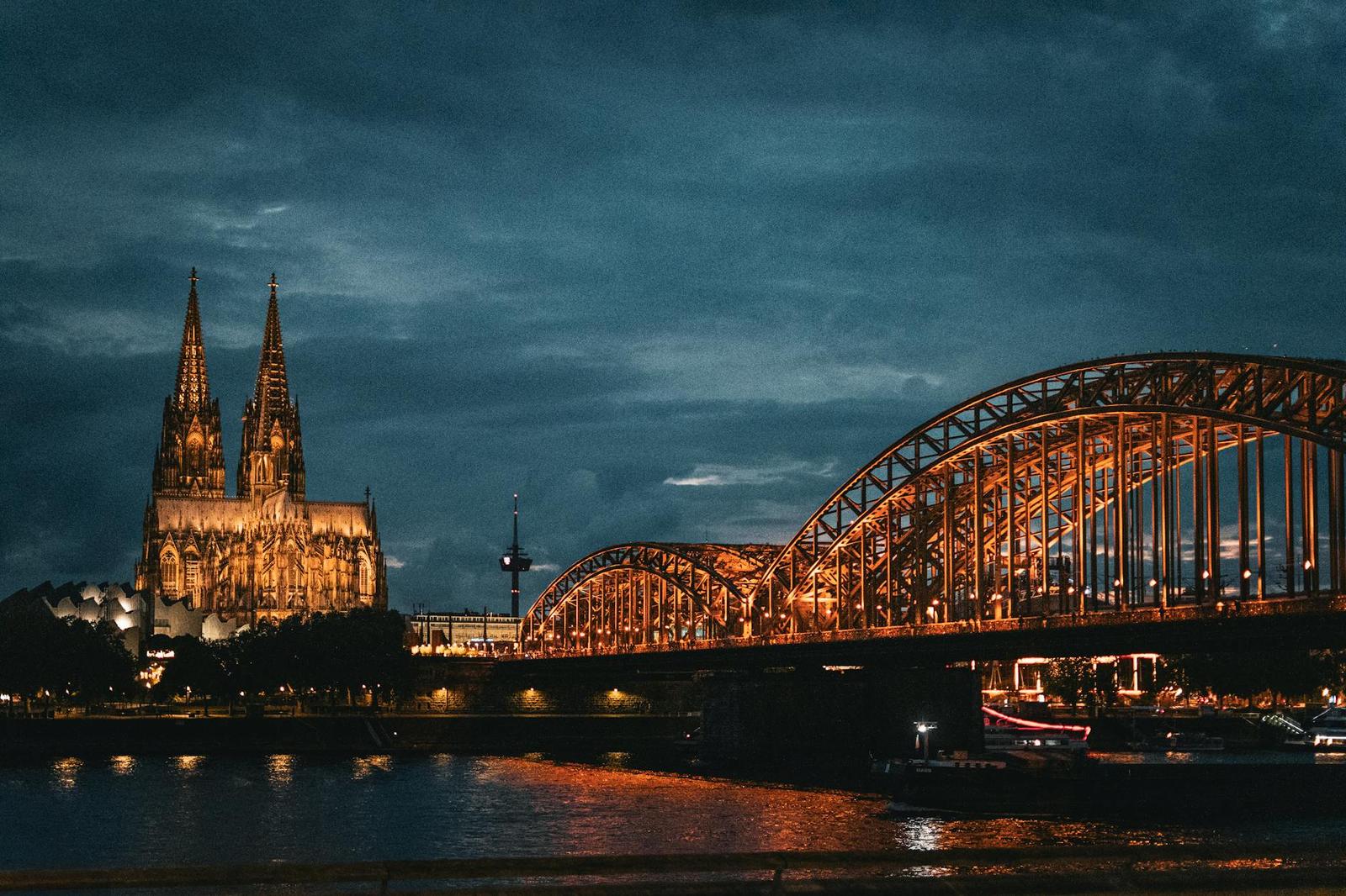 Cologne Cathedral and Hohenzollern Bridge beautifully illuminated at night reflecting over the Rhine River