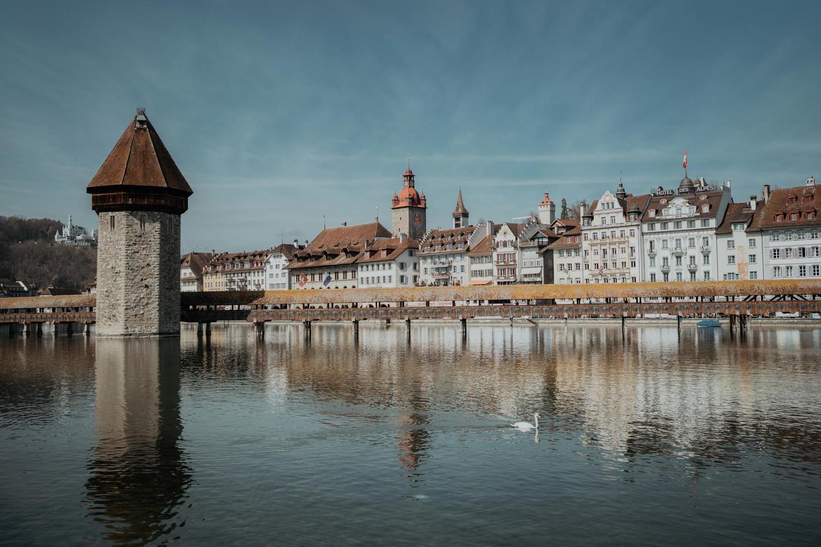Stone water tower beside a covered wooden bridge with a swan gliding on the river