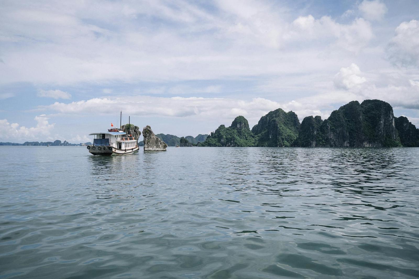 Tour boat drifting near jagged limestone peaks under a partly cloudy sky