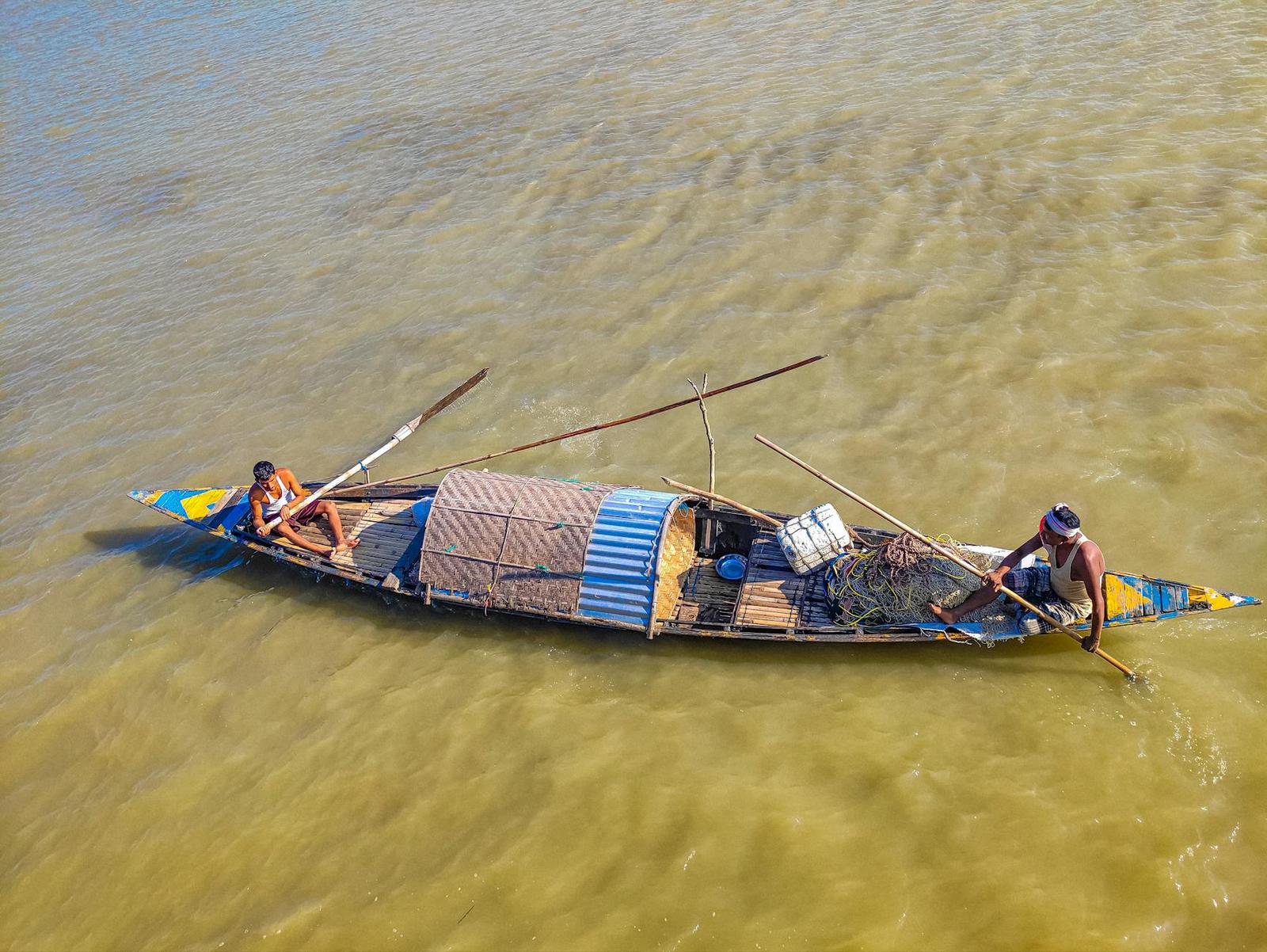 Fishermen navigate a wooden boat on the Brahmaputra River in Assam, India