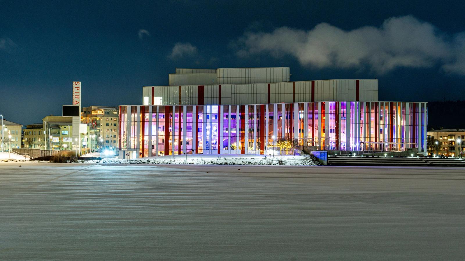 A brightly lit modern building with colorful lights, framed by snow, captured at night