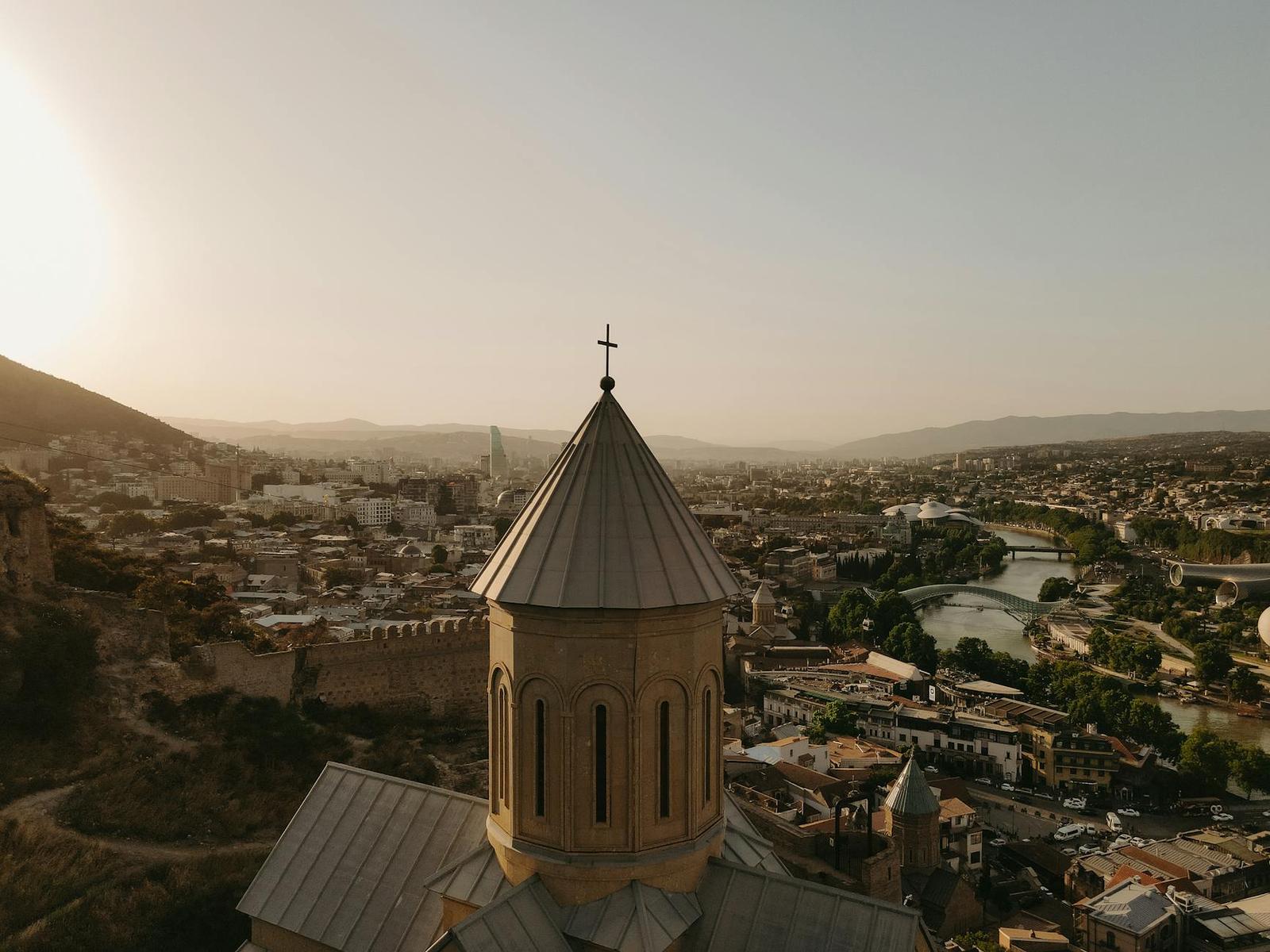 A domed church tower rising above a river valley city at golden hour