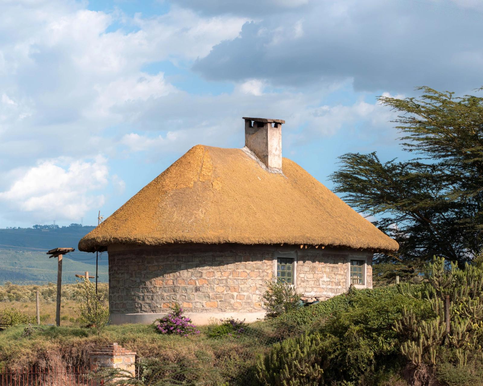 A picturesque stone hut with a thatched roof in Naivasha, Kenya surrounded by nature