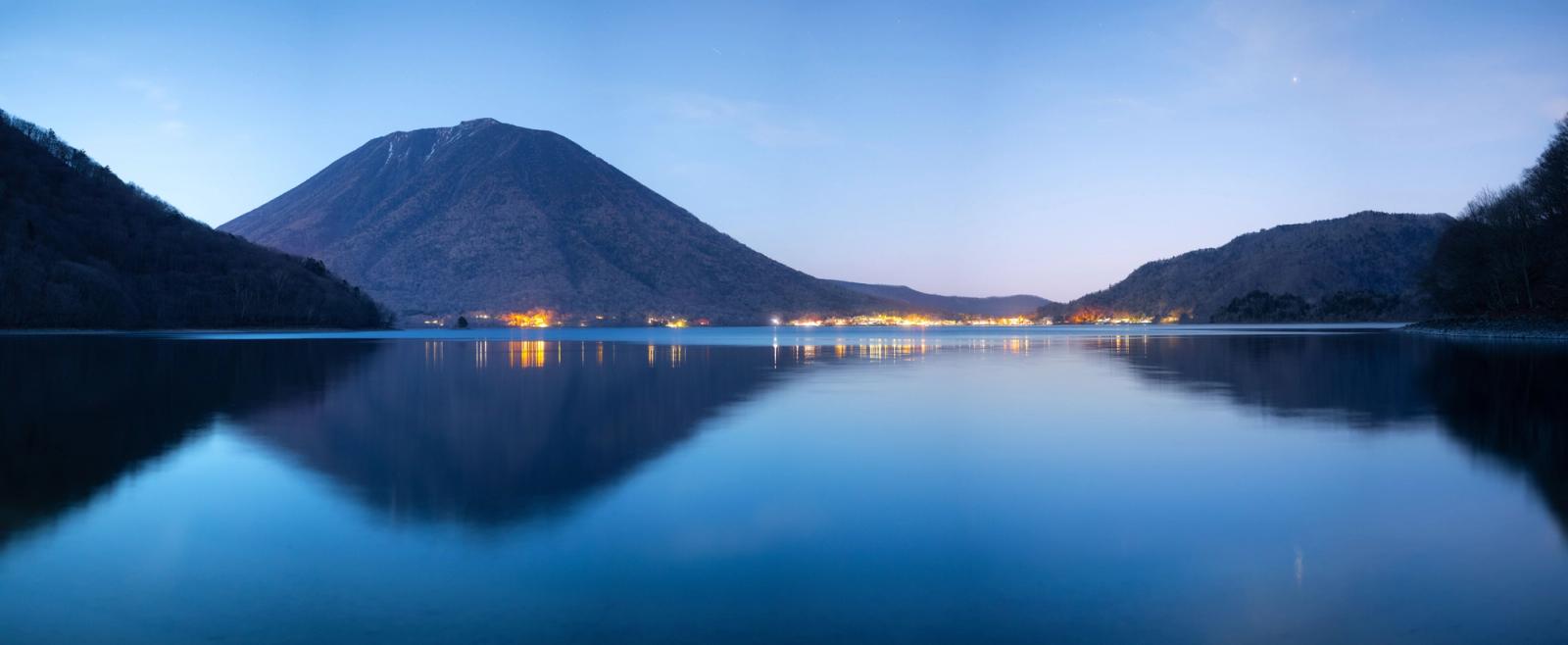 Beautiful night view of Lake Chuzenji with Mount Nantai in Nikko, Japan reflecting lights over water