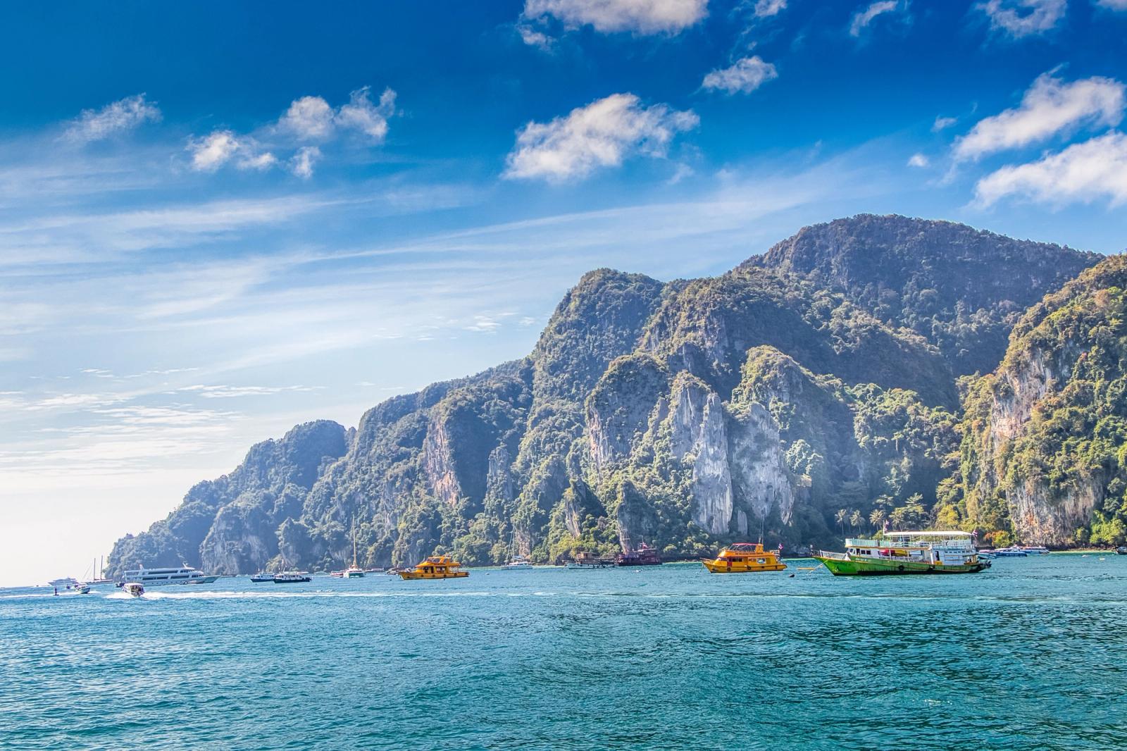 Longtail boats anchored beneath towering limestone cliffs on a bay