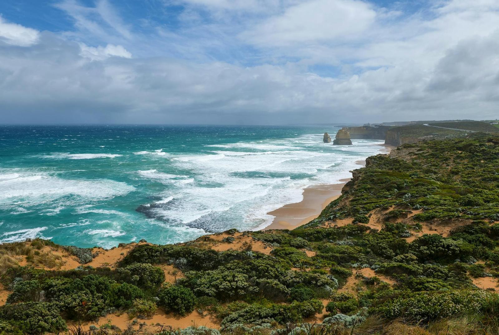 Turquoise waves break along rugged coastal cliffs under a partly cloudy sky
